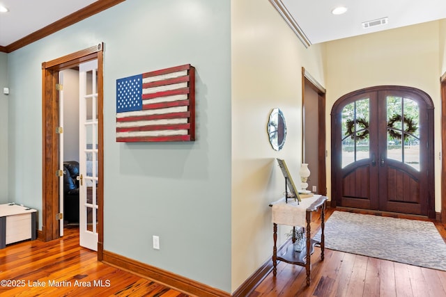 foyer entrance with arched walkways, french doors, ornamental molding, baseboards, and hardwood / wood-style flooring