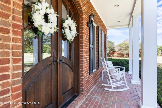 property entrance with covered porch, french doors, and brick siding