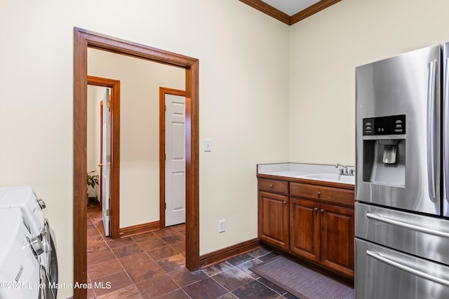 kitchen featuring baseboards, washer and clothes dryer, light countertops, stainless steel refrigerator with ice dispenser, and a sink