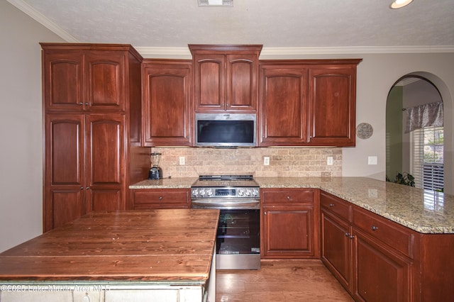 kitchen featuring light stone counters, stainless steel appliances, a peninsula, crown molding, and decorative backsplash