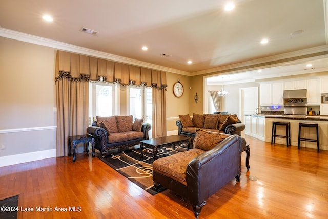 living room with sink, light hardwood / wood-style floors, crown molding, and a notable chandelier