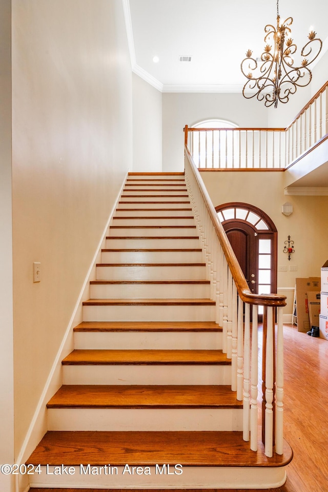 staircase with an inviting chandelier, wood-type flooring, and ornamental molding