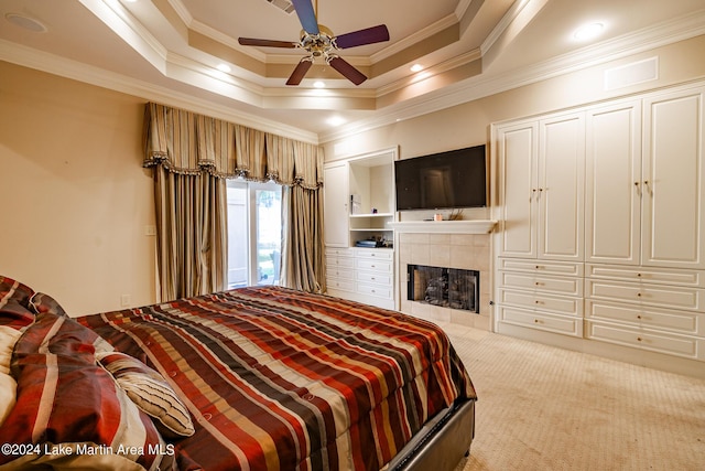 carpeted bedroom with ceiling fan, a raised ceiling, crown molding, and a tiled fireplace