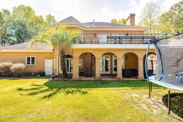 back of property with a lawn, a trampoline, and a patio