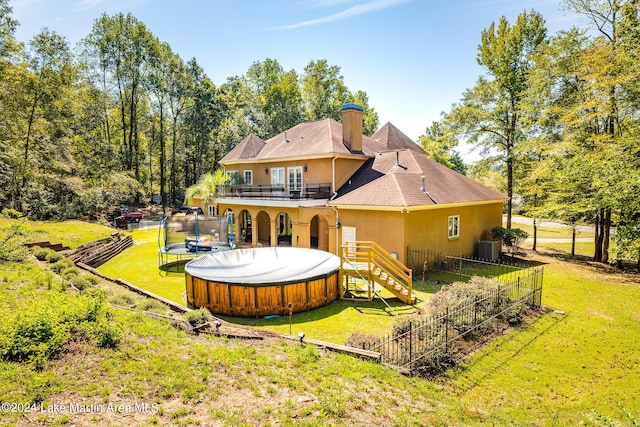 rear view of house featuring a yard, a trampoline, a balcony, and a swimming pool