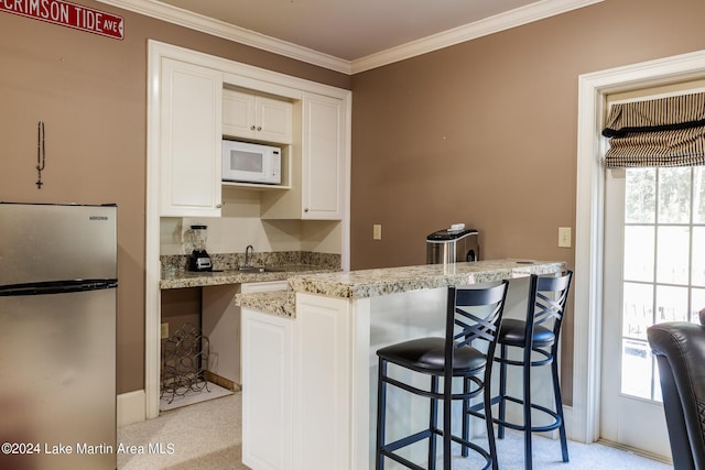 kitchen featuring white cabinetry, stainless steel fridge, crown molding, and light stone counters