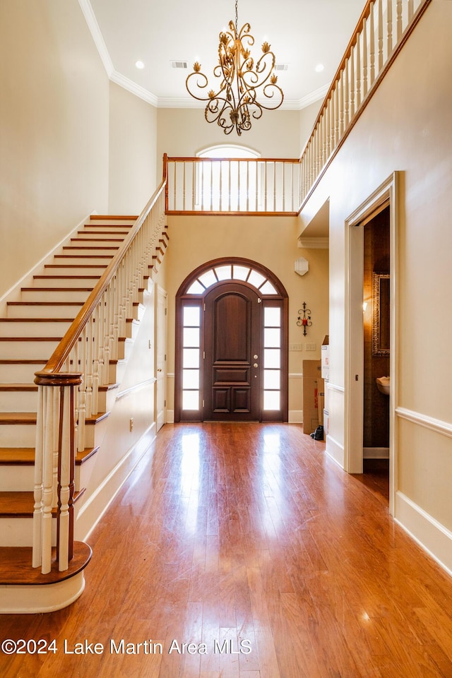 foyer entrance featuring a chandelier, a towering ceiling, hardwood / wood-style flooring, and crown molding