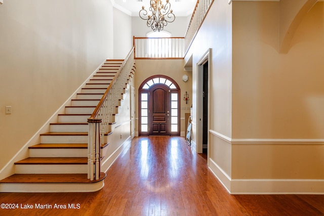 entrance foyer with crown molding, hardwood / wood-style floors, a towering ceiling, and an inviting chandelier