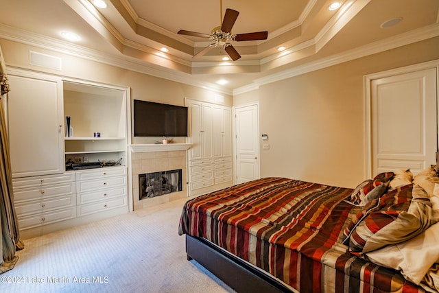 carpeted bedroom featuring ceiling fan, a raised ceiling, ornamental molding, and a tile fireplace