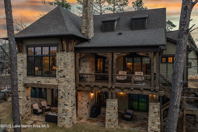 back house at dusk featuring a patio and a balcony