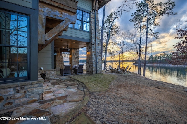 yard at dusk with a fire pit, a patio area, ceiling fan, and a water view