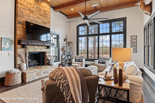 living room featuring beam ceiling, a towering ceiling, wood-type flooring, a stone fireplace, and wooden ceiling