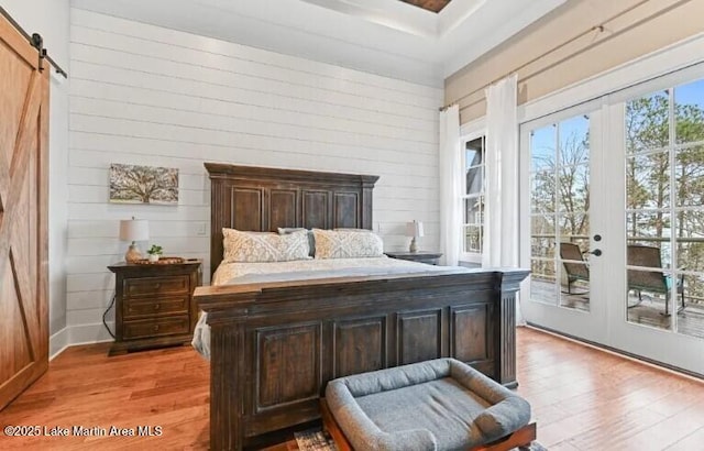 bedroom with light hardwood / wood-style floors, a barn door, access to outside, french doors, and wood walls