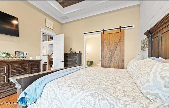 bedroom featuring hardwood / wood-style flooring, a barn door, a raised ceiling, and ensuite bathroom