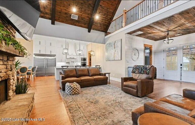 living room with high vaulted ceiling, a notable chandelier, light hardwood / wood-style floors, a stone fireplace, and wooden ceiling