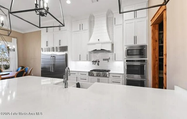 kitchen featuring built in appliances, sink, custom range hood, and white cabinets