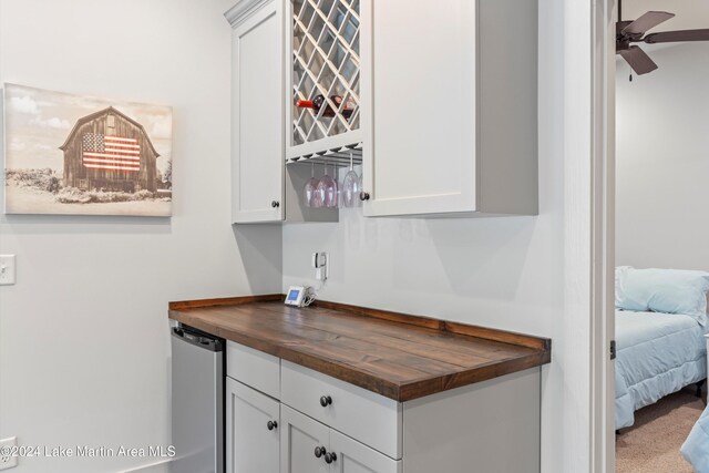 bar with wood counters, ceiling fan, dishwasher, white cabinets, and carpet floors