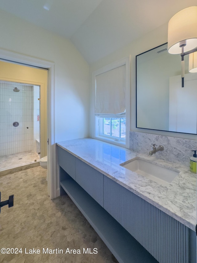 bathroom with vanity, lofted ceiling, a tile shower, and toilet