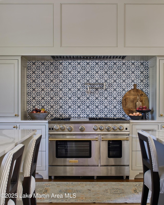 kitchen with light stone counters, tasteful backsplash, and range with two ovens