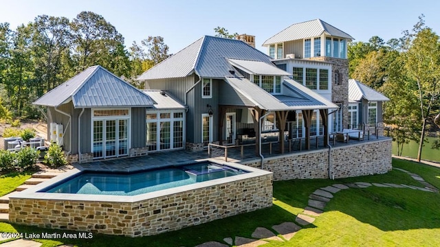 back of property featuring french doors, an in ground hot tub, a chimney, and metal roof