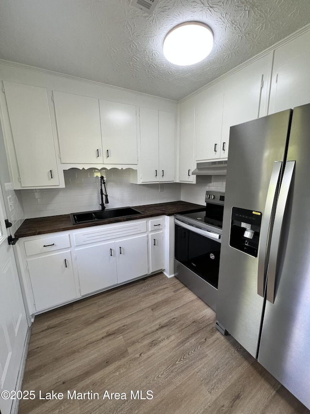 kitchen with light wood-type flooring, white cabinetry, under cabinet range hood, appliances with stainless steel finishes, and a sink