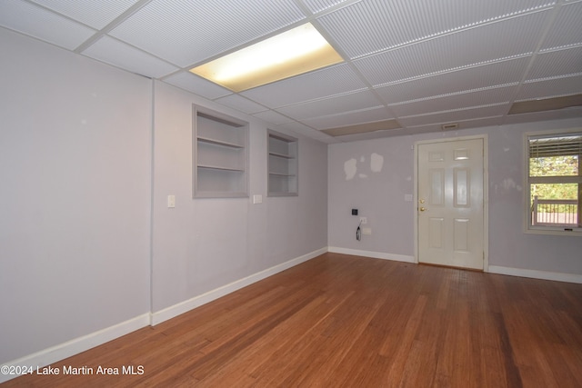 empty room with hardwood / wood-style floors, a paneled ceiling, and built in features