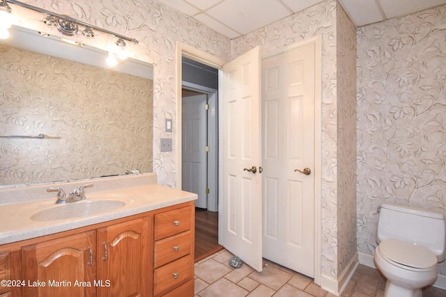 bathroom featuring tile patterned floors, a drop ceiling, toilet, and vanity