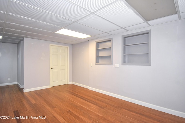 basement with hardwood / wood-style floors, a drop ceiling, and built in features