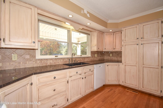 kitchen with dishwasher, dark stone counters, crown molding, sink, and light hardwood / wood-style flooring