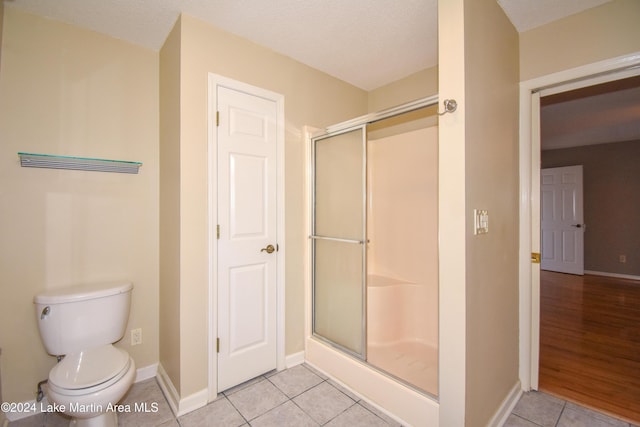 bathroom with toilet, an enclosed shower, wood-type flooring, and a textured ceiling