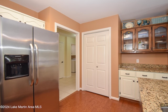 kitchen with white cabinetry, light stone counters, stainless steel refrigerator with ice dispenser, washer / clothes dryer, and light hardwood / wood-style floors