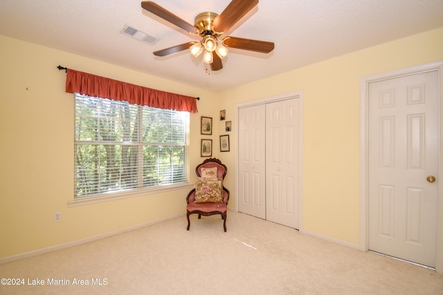 living area featuring ceiling fan, light colored carpet, and a textured ceiling