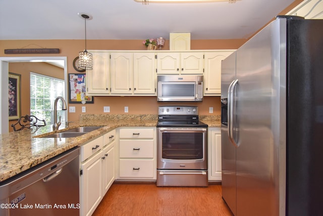 kitchen with white cabinetry, sink, hanging light fixtures, stainless steel appliances, and light wood-type flooring