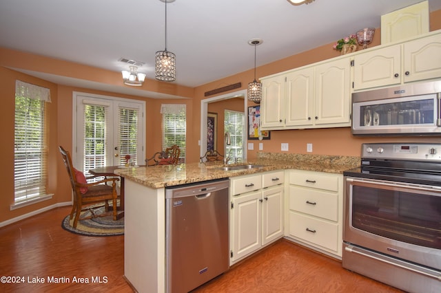 kitchen featuring stainless steel appliances, light stone counters, kitchen peninsula, light hardwood / wood-style floors, and decorative light fixtures