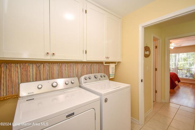 clothes washing area featuring cabinets, light tile patterned floors, and washing machine and clothes dryer