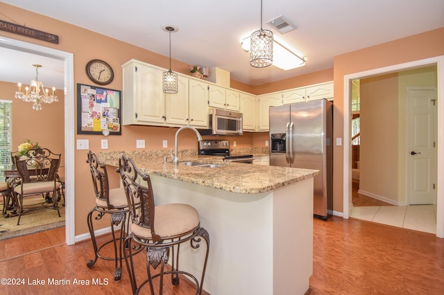 kitchen with sink, light hardwood / wood-style flooring, a notable chandelier, kitchen peninsula, and appliances with stainless steel finishes