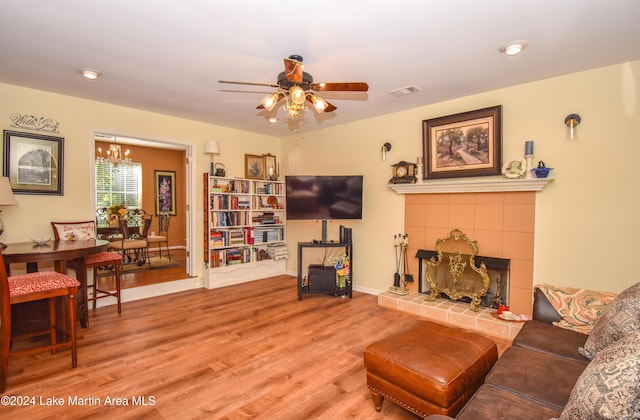 living room featuring a tiled fireplace, wood-type flooring, and ceiling fan with notable chandelier