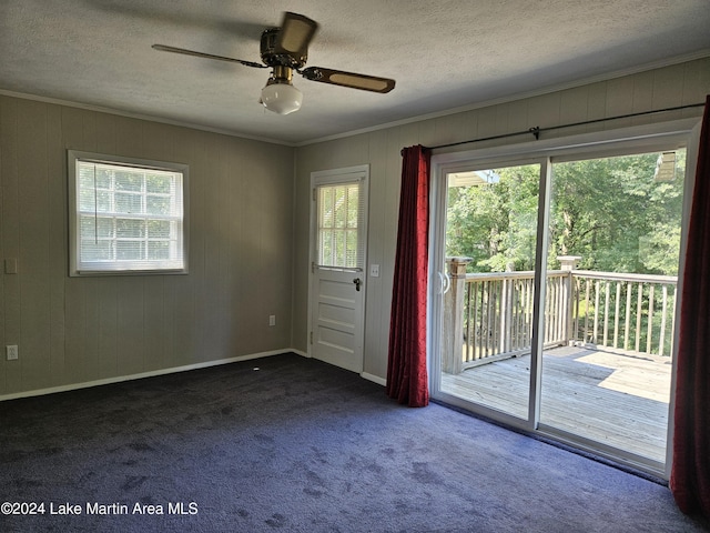 carpeted spare room with ceiling fan, wood walls, ornamental molding, and a textured ceiling