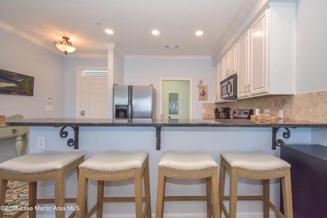 kitchen featuring white cabinetry, ornamental molding, appliances with stainless steel finishes, decorative backsplash, and dark stone counters