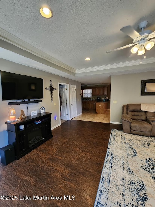 living room featuring light hardwood / wood-style flooring, ornamental molding, a raised ceiling, and a textured ceiling