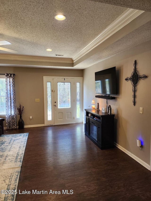 foyer with ornamental molding, dark hardwood / wood-style flooring, a raised ceiling, and a textured ceiling