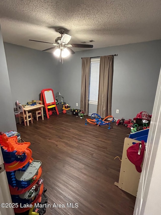 playroom featuring ceiling fan, dark hardwood / wood-style flooring, and a textured ceiling