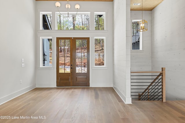 foyer with a notable chandelier, wood finished floors, baseboards, visible vents, and a towering ceiling