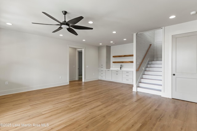 unfurnished living room with a sink, stairway, light wood finished floors, and recessed lighting