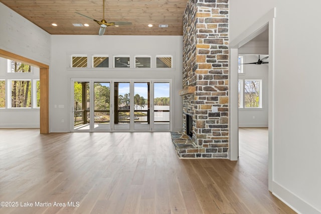 unfurnished living room with a stone fireplace, ceiling fan, a high ceiling, and wood finished floors
