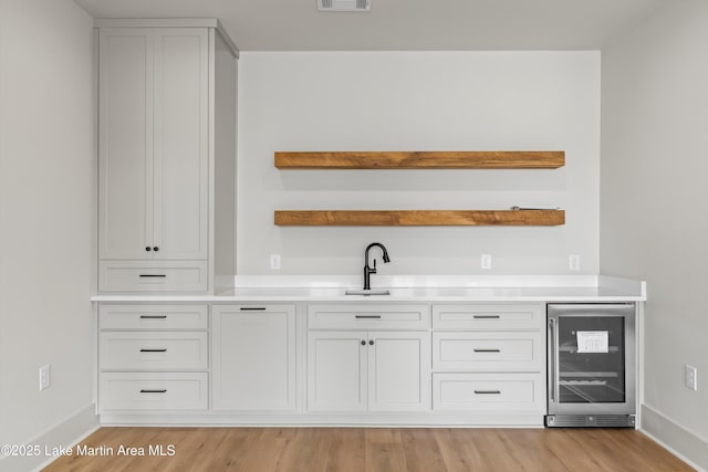 bar featuring baseboards, beverage cooler, visible vents, light wood-style flooring, and indoor wet bar