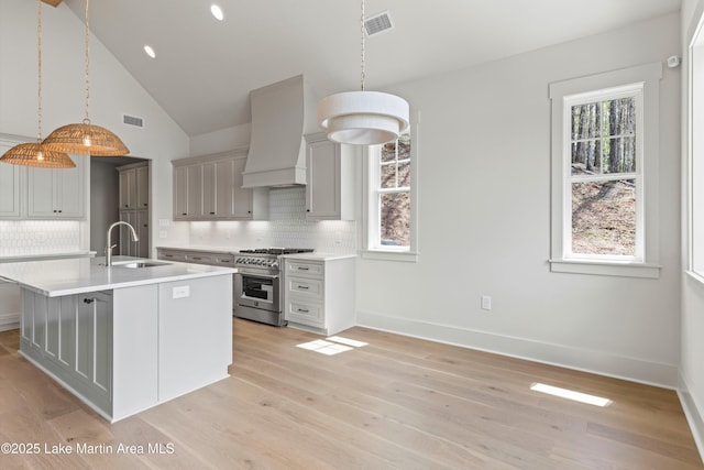 kitchen featuring light countertops, a sink, visible vents, custom range hood, and stainless steel stove