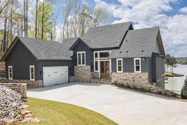 view of front of home featuring stone siding, a water view, an attached garage, board and batten siding, and driveway