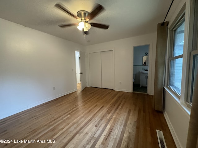 unfurnished bedroom with ensuite bathroom, light hardwood / wood-style flooring, multiple windows, and ceiling fan