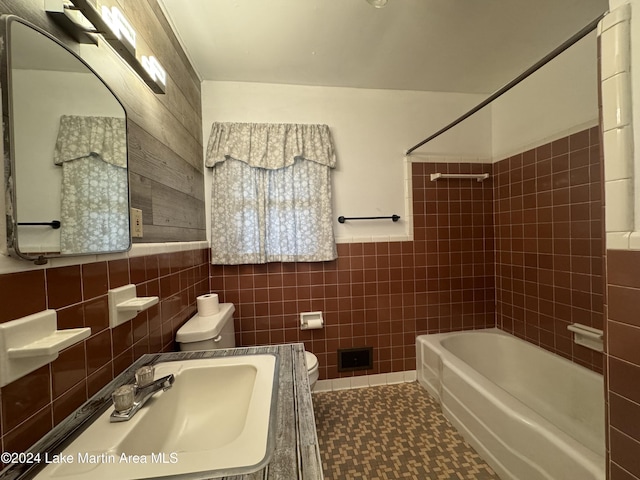 full bathroom with tiled shower / bath, toilet, tile walls, and sink